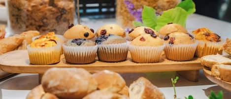 Diverse gebakjes op een houten plank, waaronder muffins en gebak, met twee potten granola op de achtergrond.