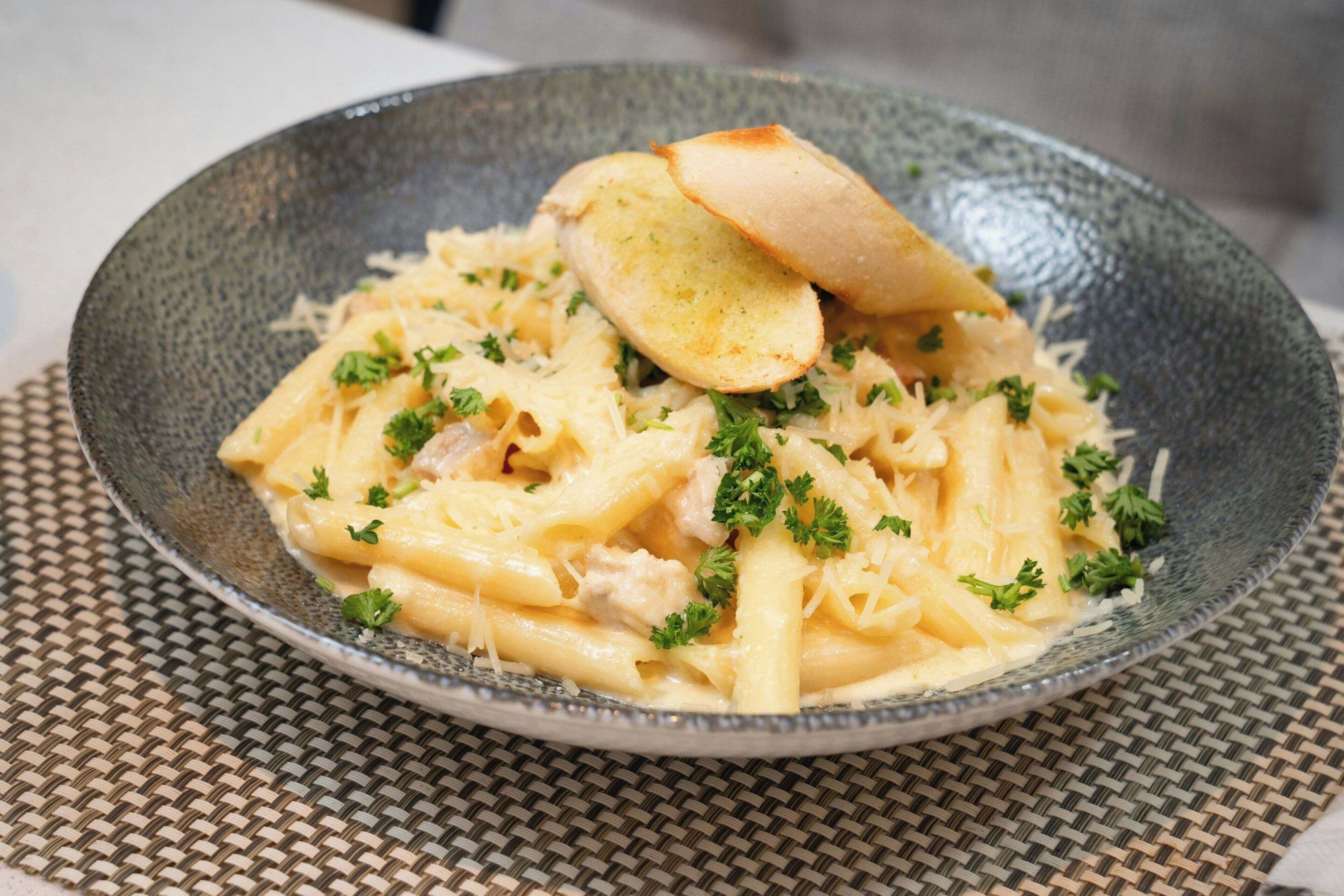 Un plato de pasta con pan sobre un camino de mesa tejido.