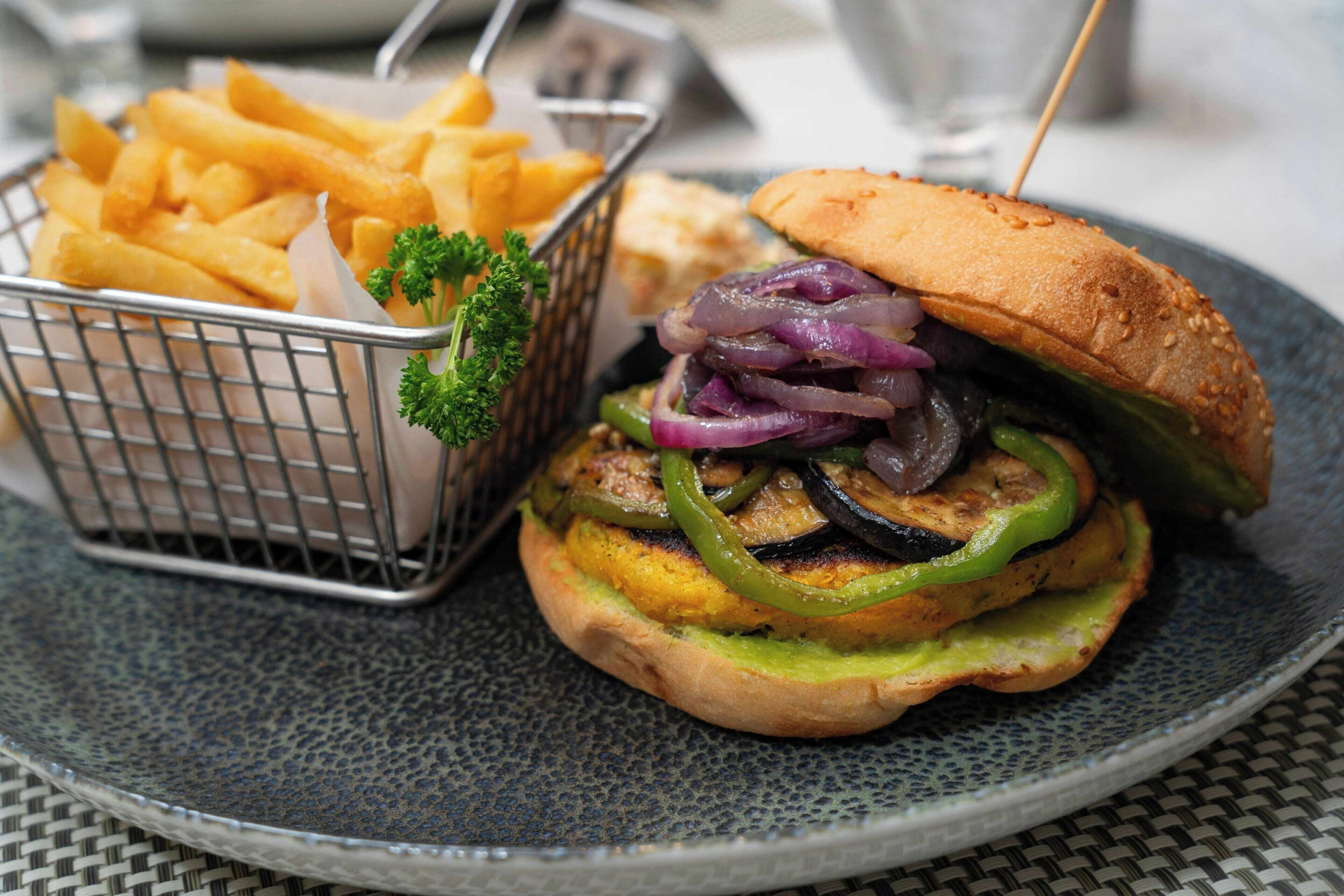 A burger with a sesame seed bun, grilled vegetables, and a side of French fries.