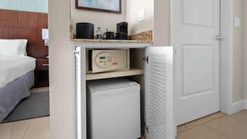 A hotel room with a bed, a small refrigerator, a microwave, and a coffee maker on the countertop.