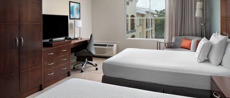A hotel room with two beds, a desk with a computer, a TV, and a window with curtains.