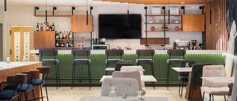 Un restaurant moderne doté d’un bar, de tables et d’un grand écran de télévision.