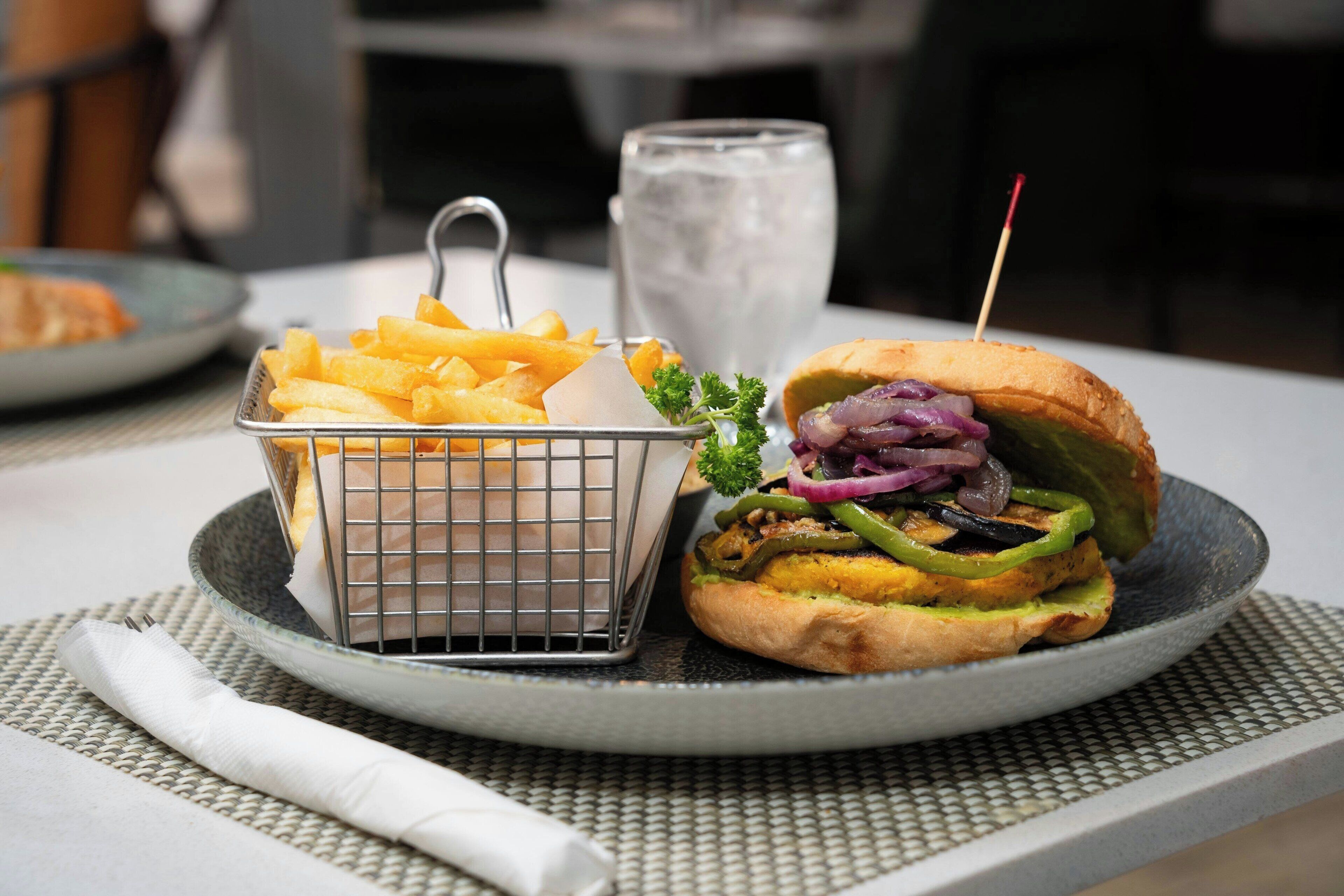 A meal consisting of a burger with various toppings and a basket of fries, served on a plate with a glass of water.