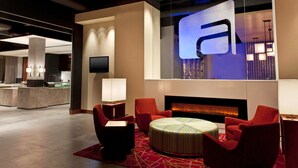Eine moderne Lobby mit Kamin, roten Sesseln, einem runden Hocker und einer großen, beleuchteten Leuchtreklame.