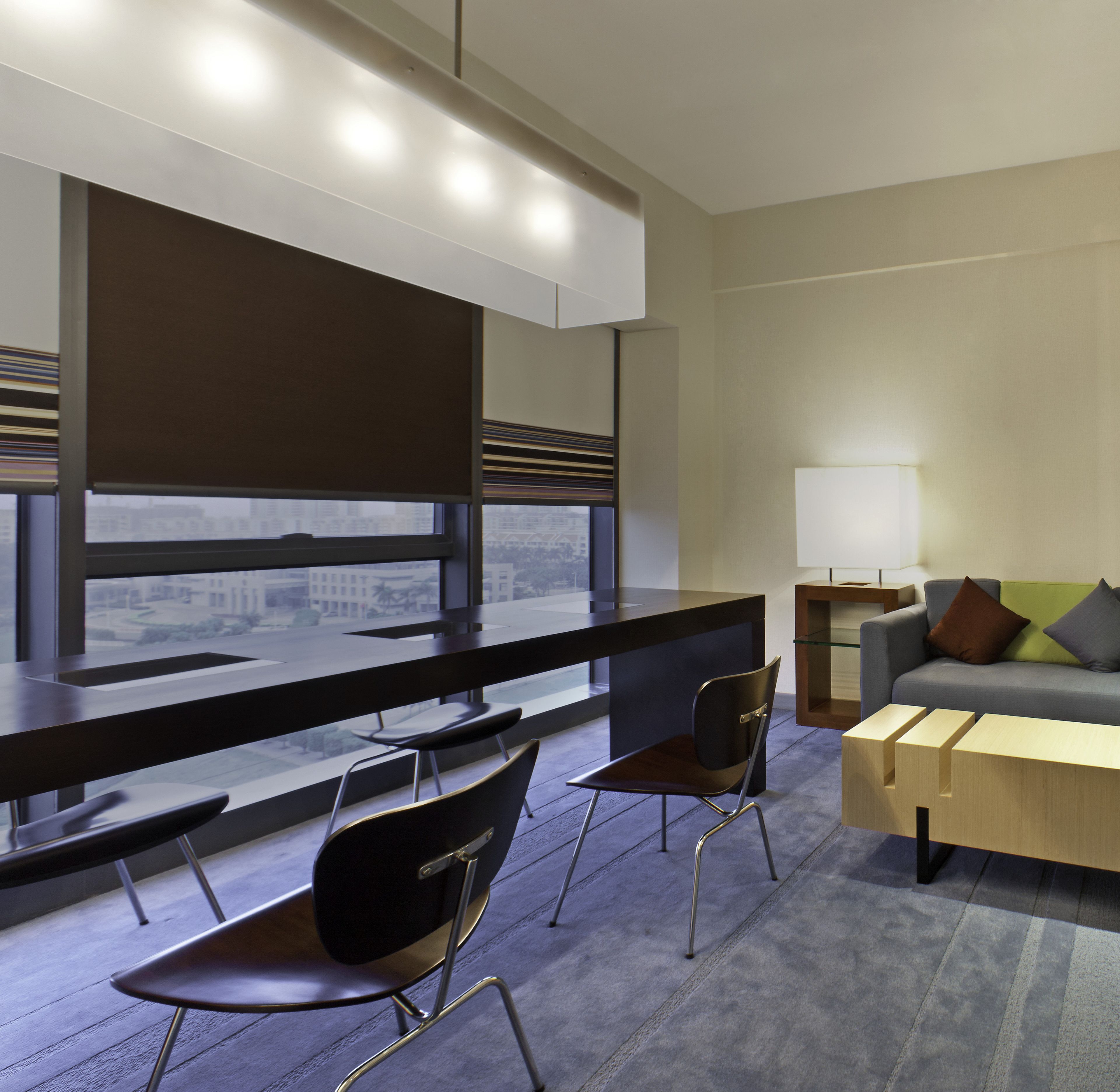 Una habitación de hotel moderna con un ventanal grande, un escritorio, dos sillas, un sofá y una lámpara.