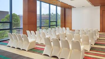 Un salón de conferencias con filas de sillas blancas, ventanas amplias y suelo alfombrado.