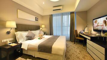 Habitación de hotel con cama, mesitas de noche, escritorio, silla, televisor y ventana con cortinas.