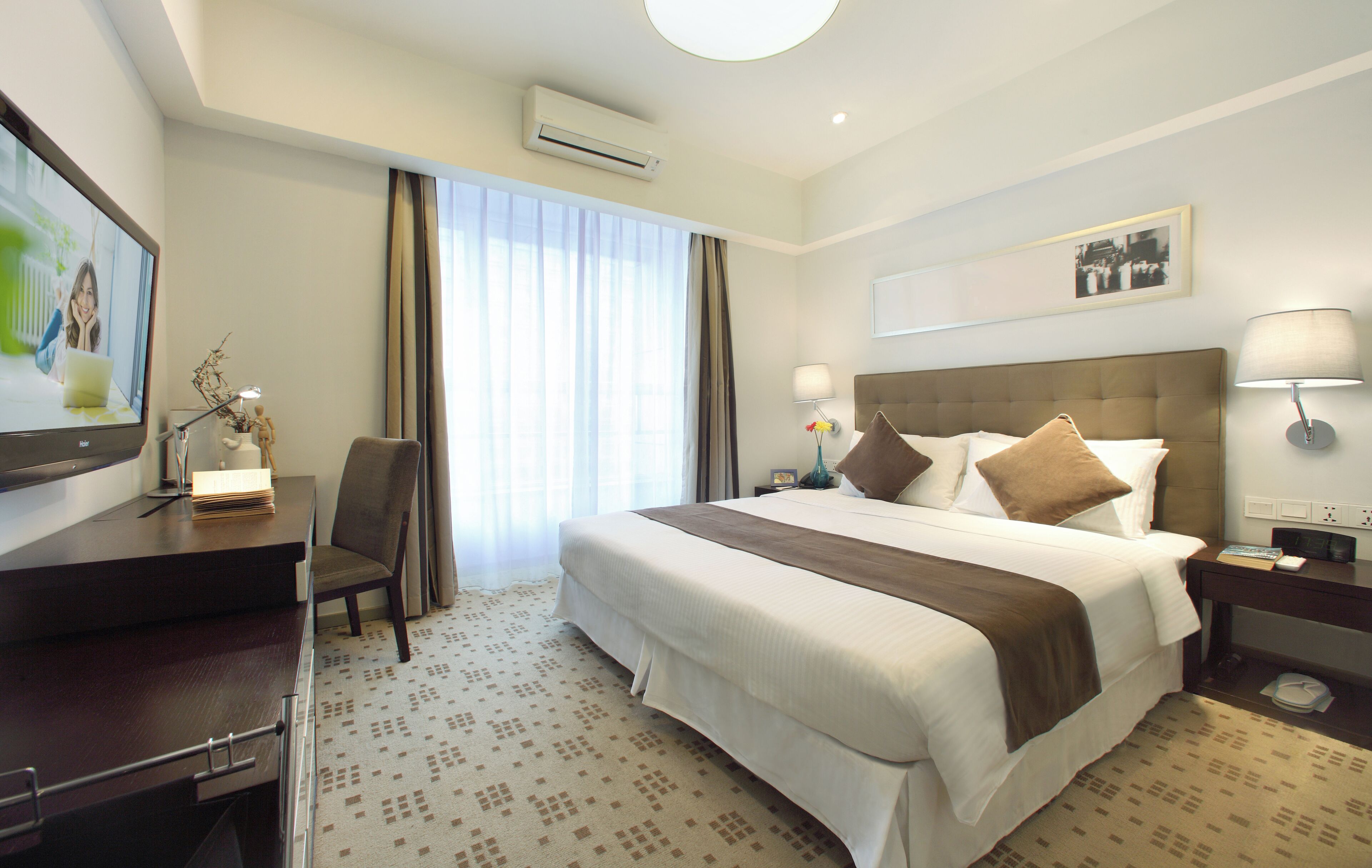 Ein Hotelzimmer mit Bett, Schreibtisch, Stuhl, Lampe und einem Kunstwerk an der Wand.