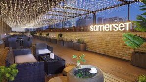 Un área de lounge en la azotea con mobiliario de mimbre, una mesa de vidrio con una planta y un letrero que dice "somerseT".