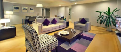 A modern living room with a sofa, armchair, coffee table, and a dining area with chairs and a table.