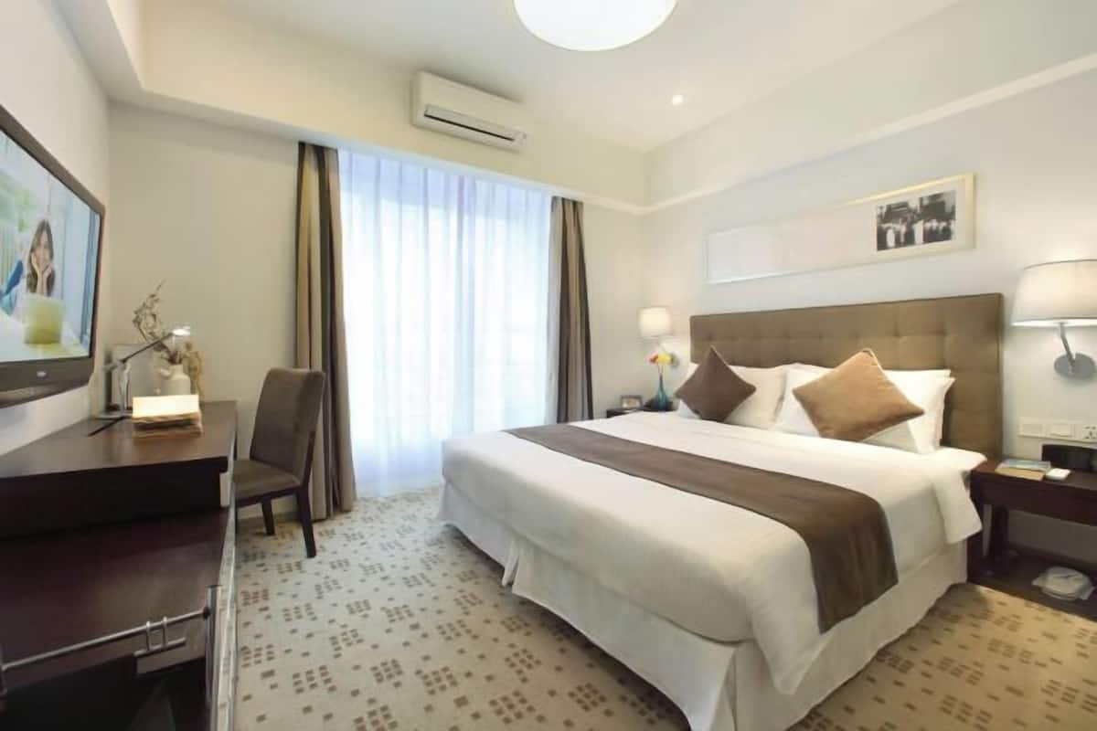 Ein Hotelzimmer mit einem großen Bett, einem Schreibtisch, einem Sessel, einem Fernseher und einem Fenster mit Vorhängen.