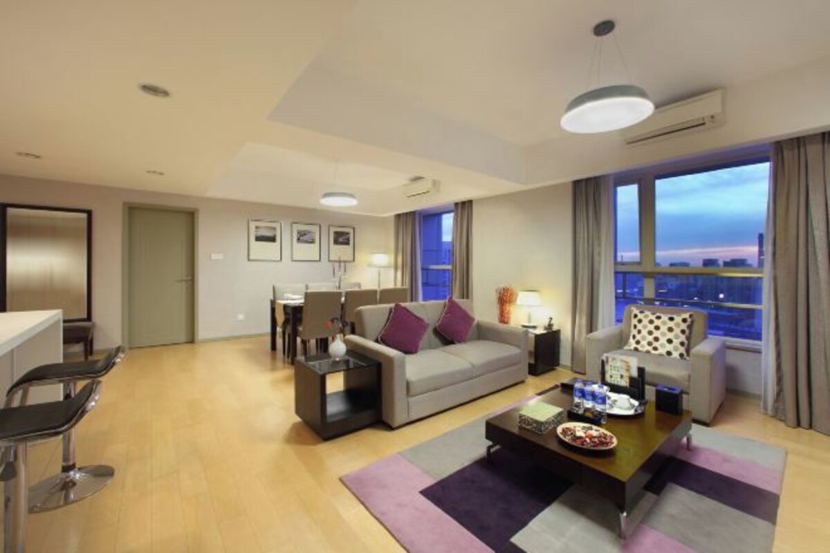 A modern hotel room with a sofa, coffee table, and dining area.