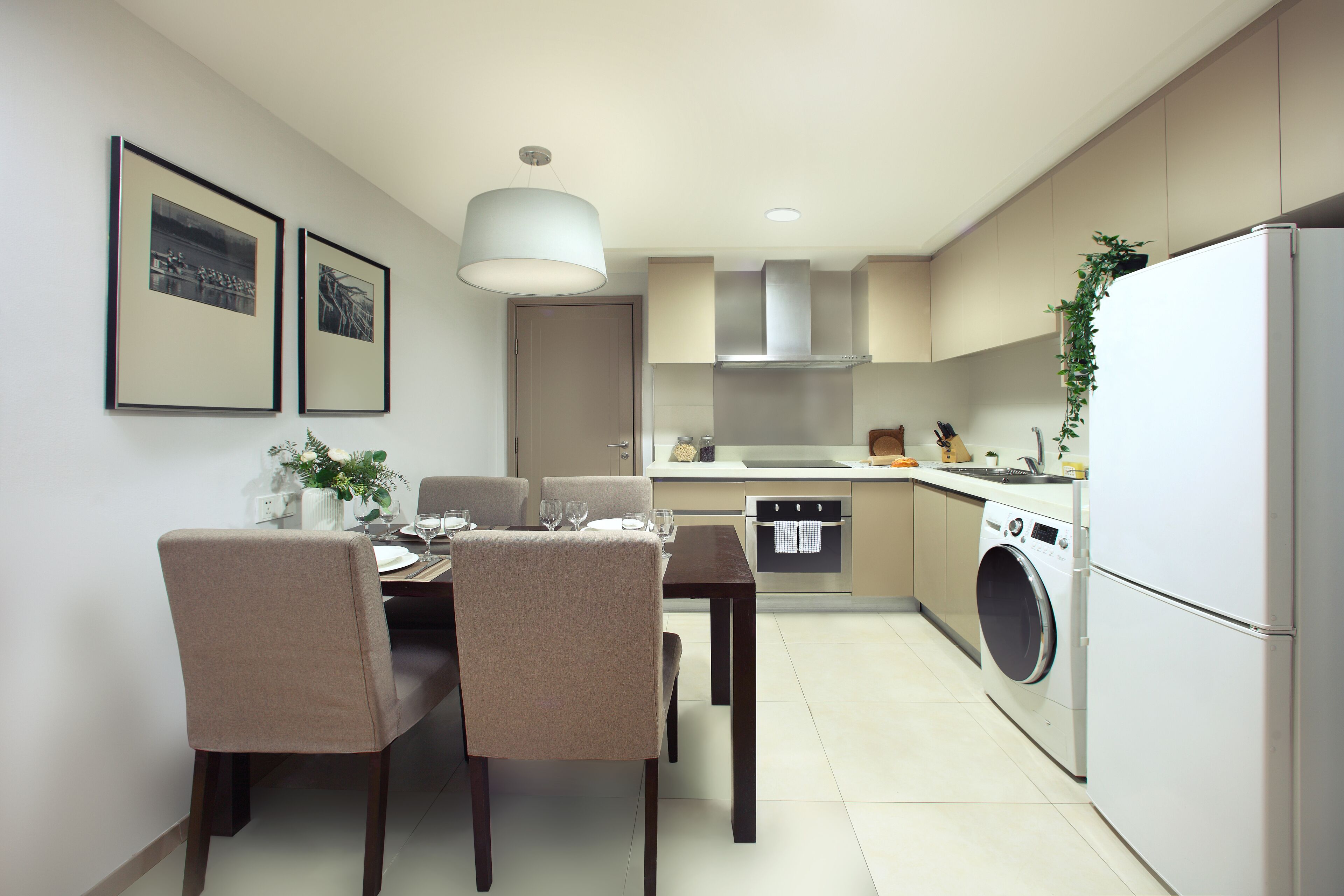 A modern kitchen with a dining area, including a table with chairs, a washing machine, and a hanging light fixture.