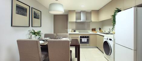 A modern kitchen with a dining area, including a table with chairs, a washing machine, and a hanging light fixture.