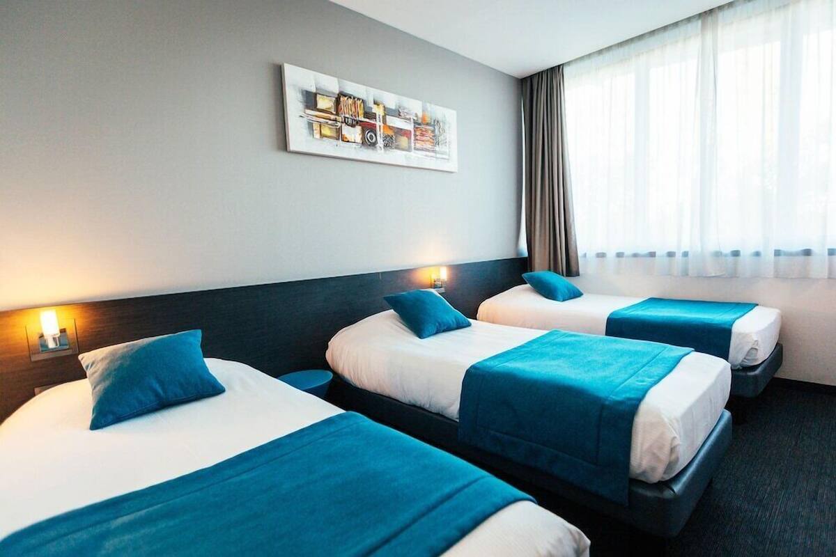 A hotel room with two beds, a headboard, a wall-mounted artwork, and a window with curtains.