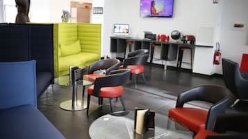 Un espace d’attente moderne avec un canapé vert, des chaises noires et rouges, une table en verre et un téléviseur fixé au mur.