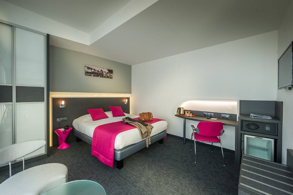 A hotel room with a bed, desk, chair, and a small kitchenette.