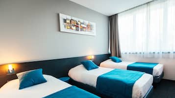 A hotel room with three beds, each with blue bedding and pillows, a large abstract painting on the wall, and a window with curtains.