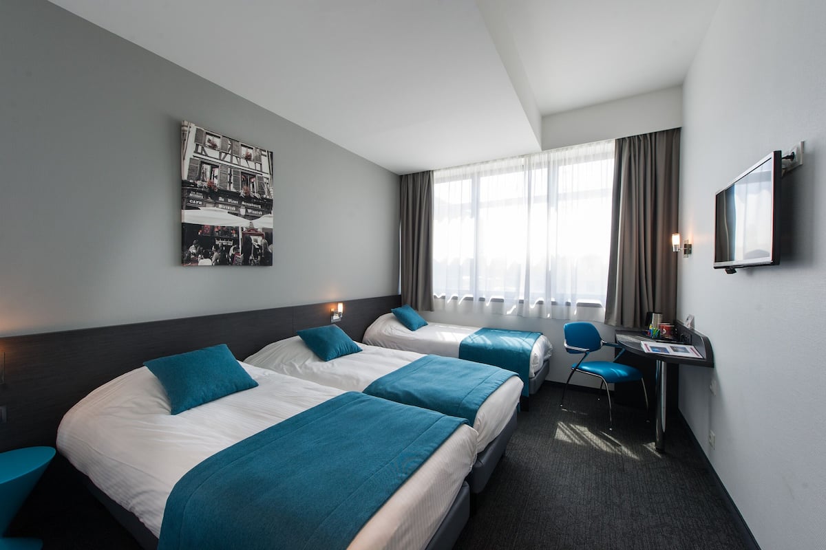 A hotel room with two beds, a desk, a chair, and a TV.