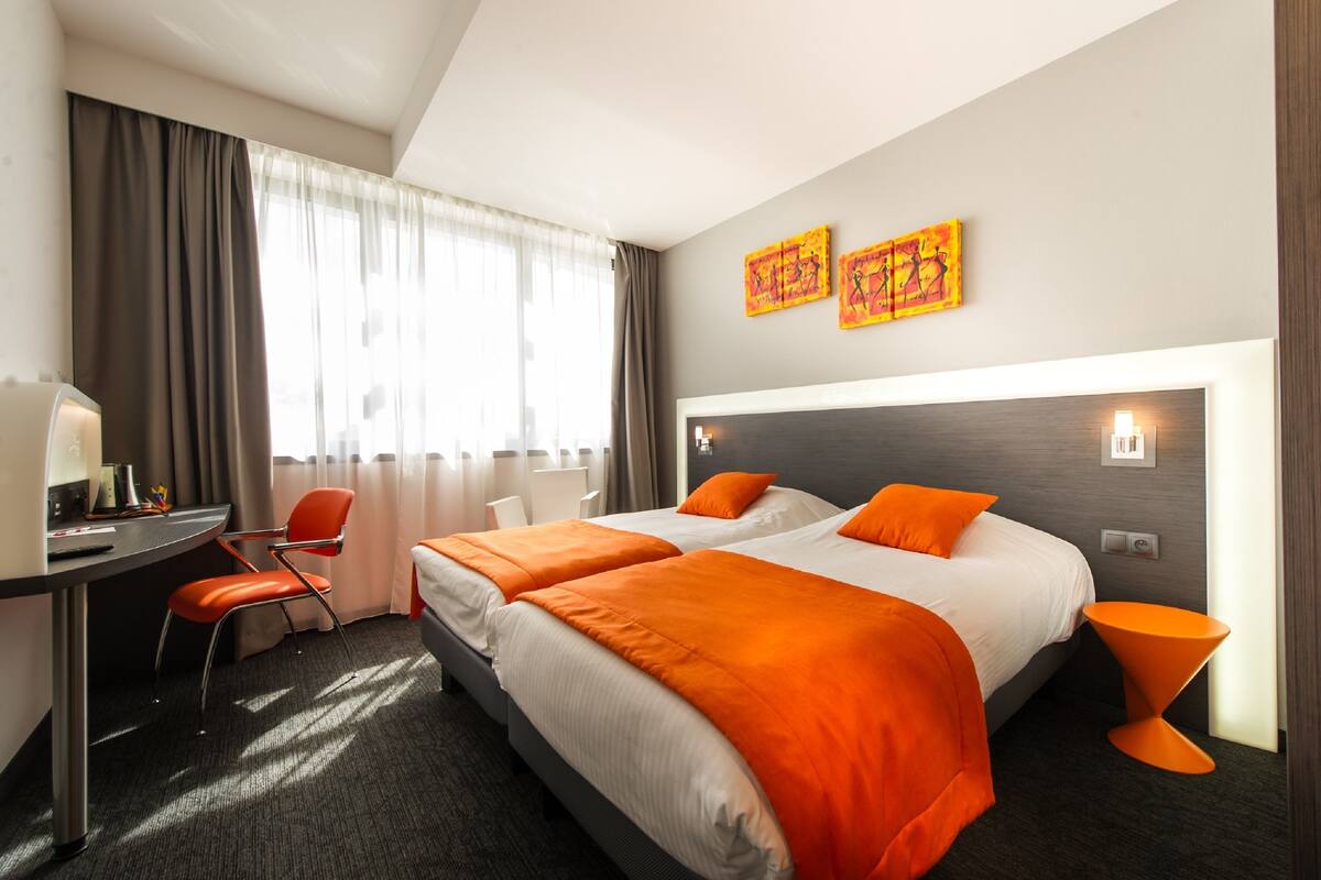 A hotel room with two beds, a desk, a chair, and artwork on the wall.