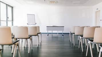 Un salón de conferencias con filas de sillas mirando una pizarra y una mesa.