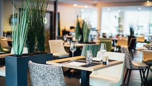 Un interior de restaurante moderno con mesas y sillas ordenadas, plantas en macetas y un ambiente limpio y bien iluminado.