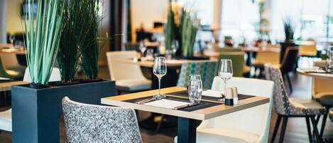 En modern restauranginteriör med snyggt placerade bord och stolar, krukväxter och en ren, väl upplyst atmosfär.