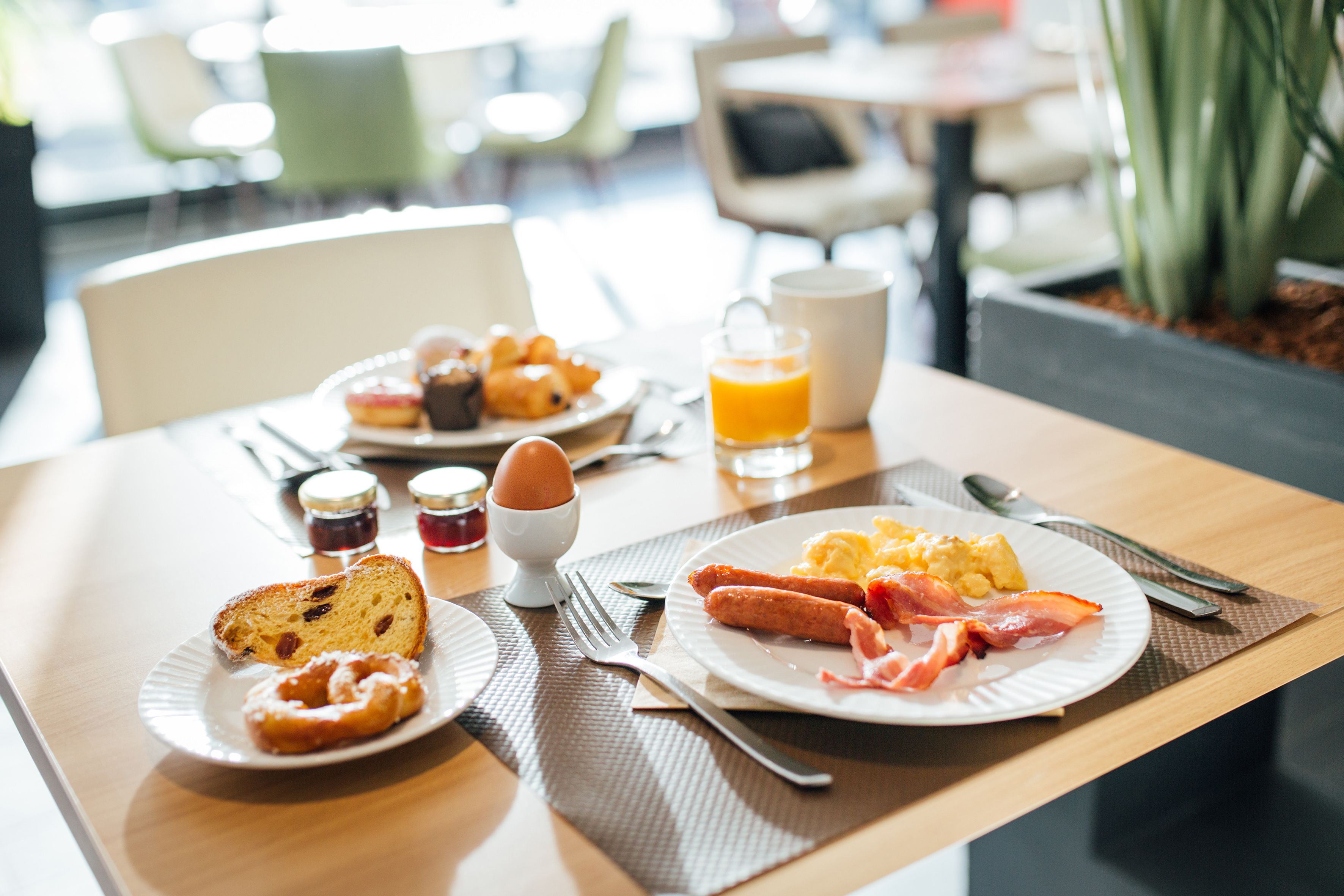 Uma mesa de café da manhã com pratos de comida, um copo de suco de laranja e acompanhamentos.