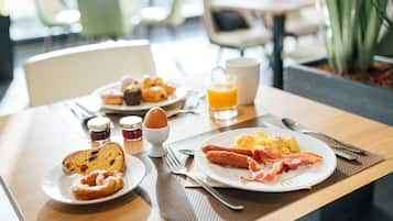 A breakfast table with plates of food, a glass of orange juice, and condiments.