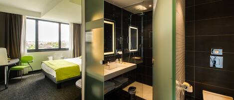 Habitación de hotel con cama, escritorio, silla y baño con inodoro, lavabo y espejo.