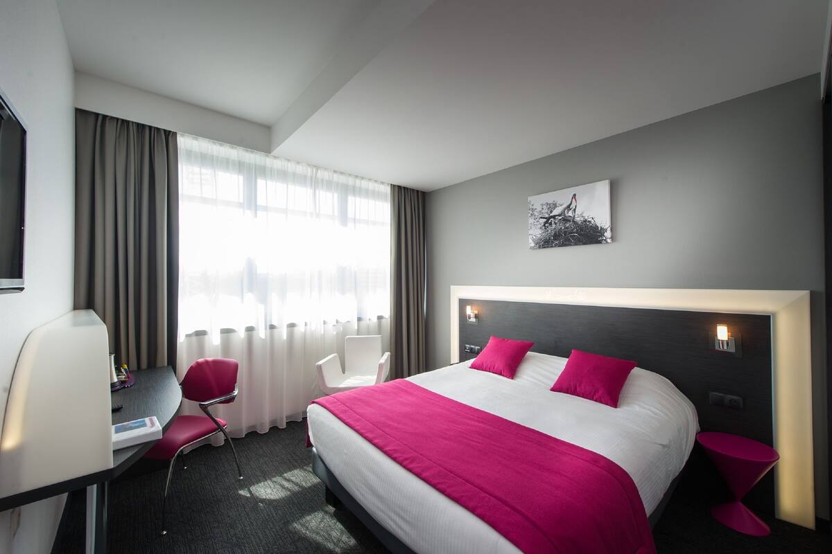 A hotel room with a bed, a desk, a chair, and a window with curtains.