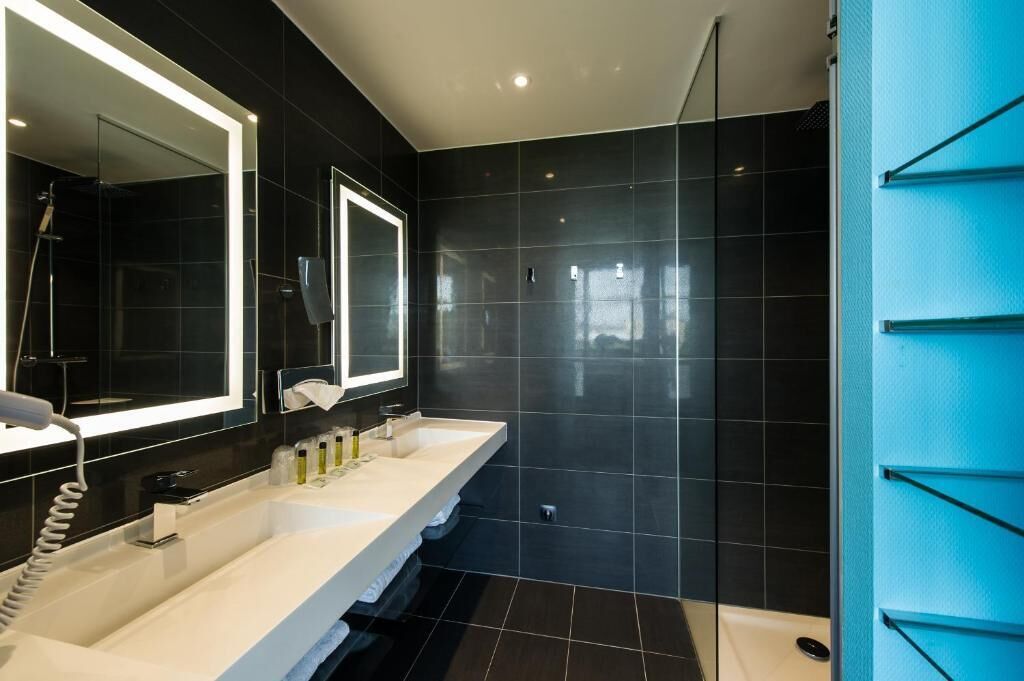 Un baño moderno con un espejo grande, dos lavamanos y una zona de ducha.