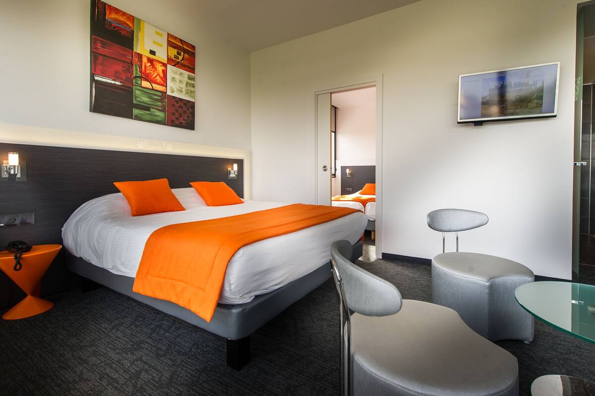 A modern hotel room with a large bed, a glass table, a chair, and a mirror.