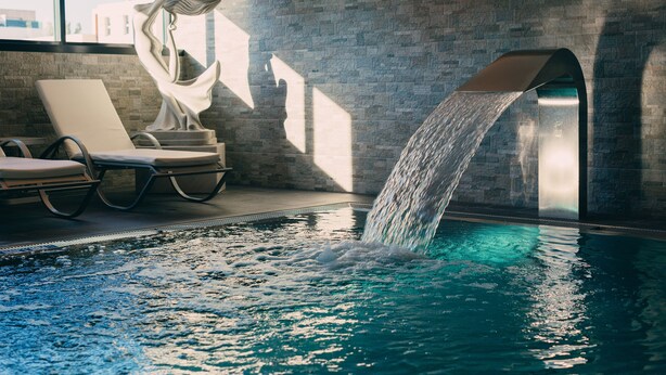 Una piscina con fuente, sillas de descanso y un muro de piedra.