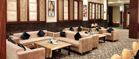 A hotel lobby with sofas and tables, decorative panels, and a patterned carpet.