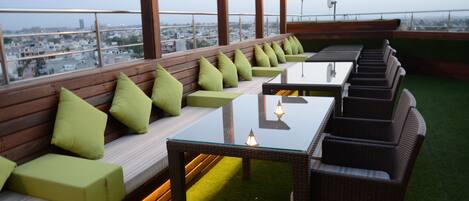 Terraza en la azotea con zonas de estar, una mesa de vidrio y vistas panorámicas de la ciudad.