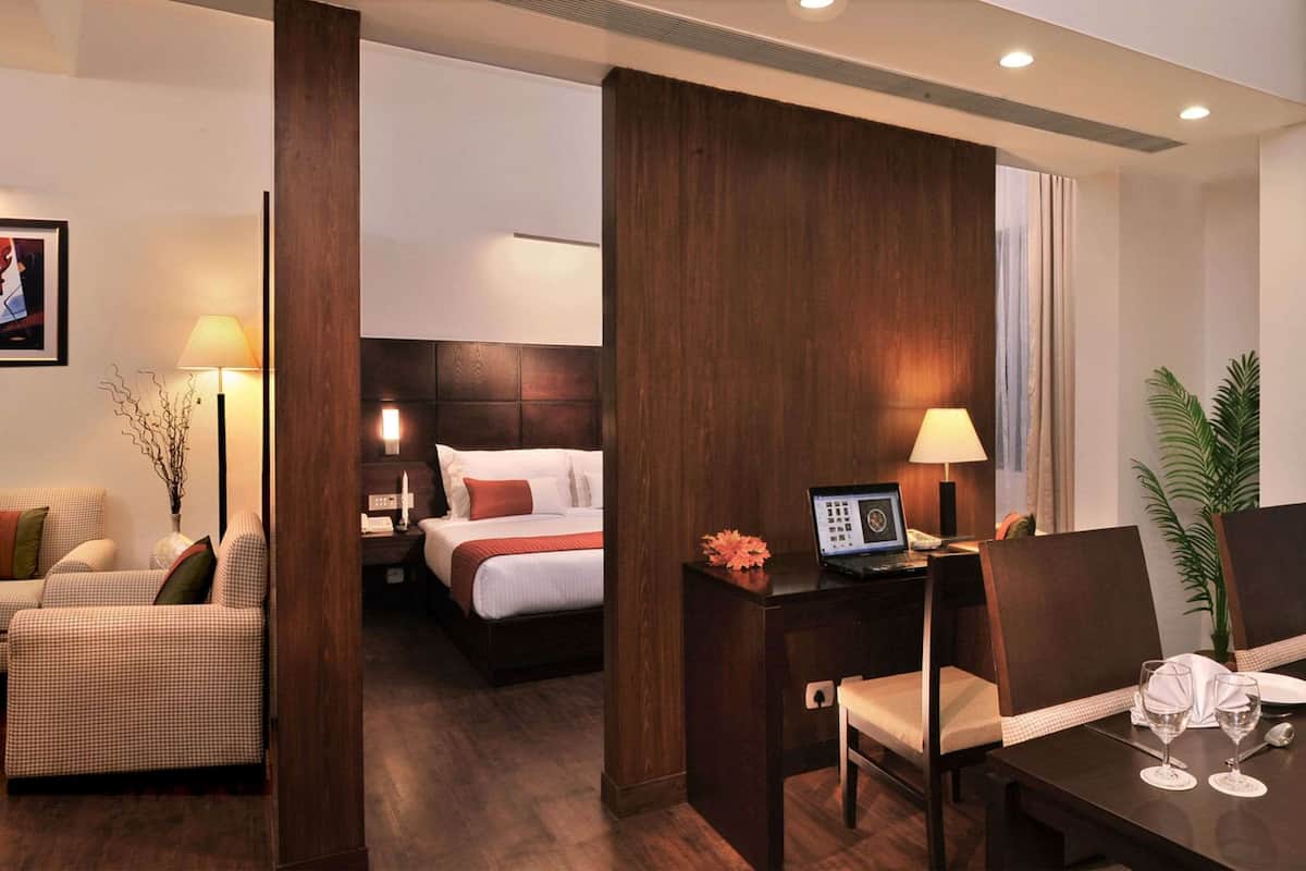 A hotel room with a bed, a desk with a computer, a dining table set for two, and a view of the city through the window.