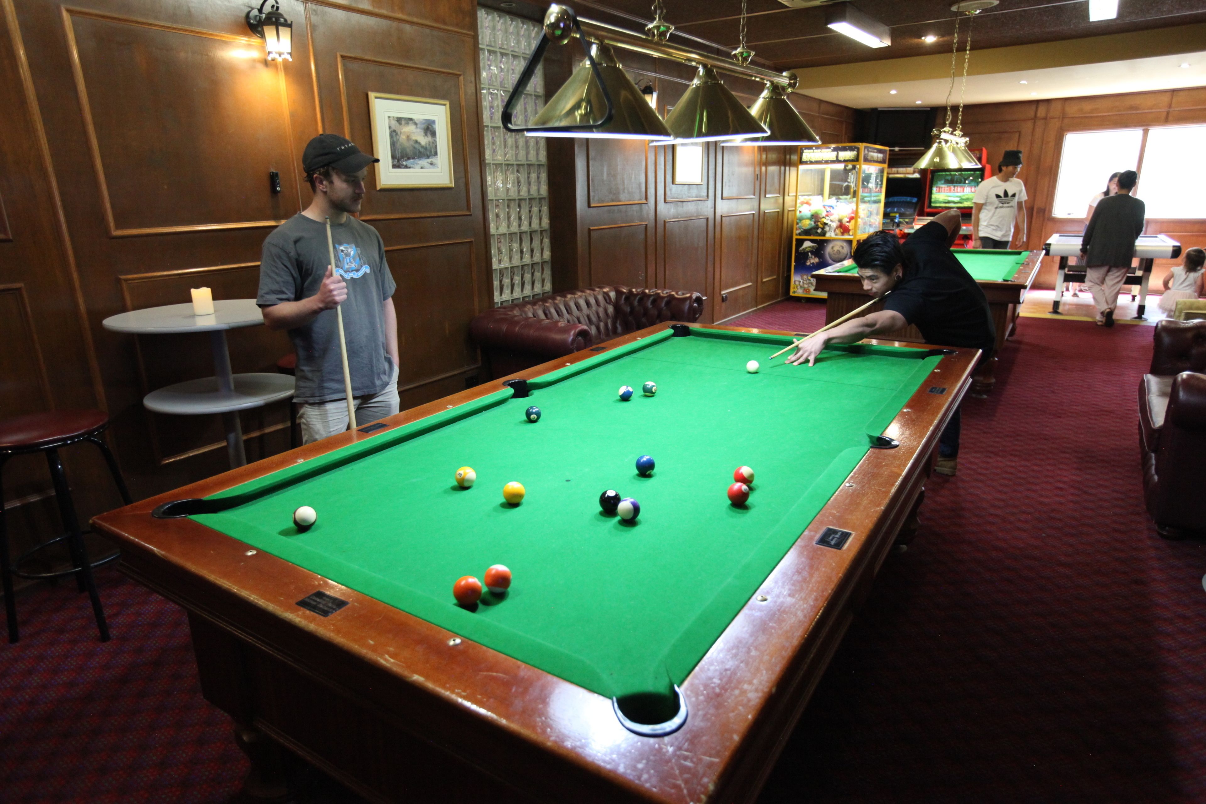 A pool table with balls, a billiard cue, and a person playing.