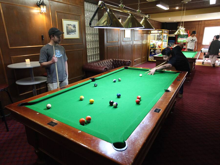 A pool table with balls, a billiard cue, and a person playing.