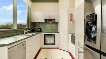 A kitchen with white cabinets, a stainless steel refrigerator, a built-in oven, and a window with a view of trees.