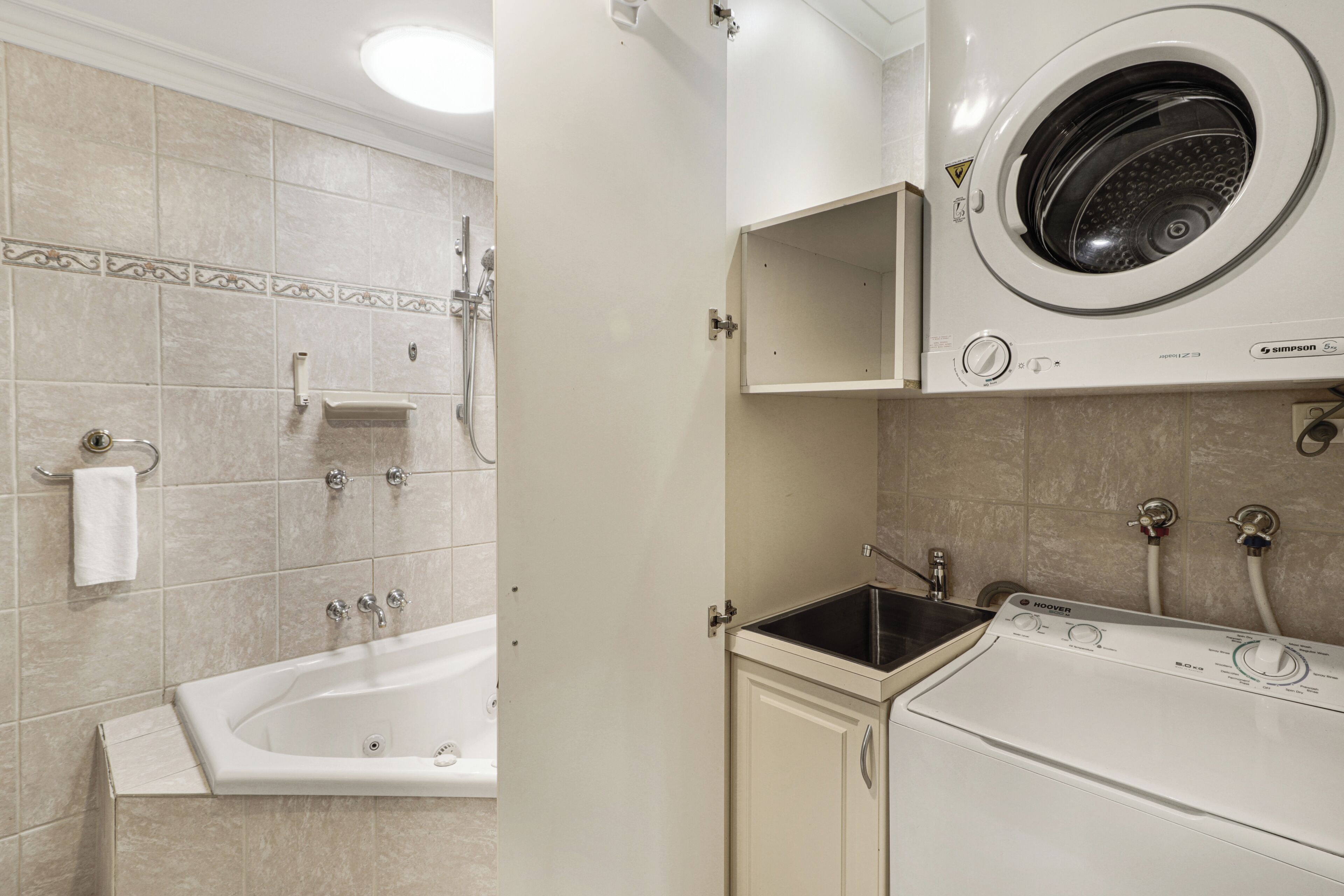 A laundry room with a front-loading washer and dryer, a sink, and a bathtub.