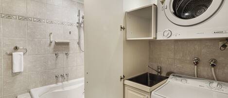 A laundry room with a front-loading washer and dryer, a sink, and a bathtub.