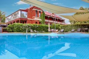 A swimming pool with lounge chairs and a building with a balcony in the background.