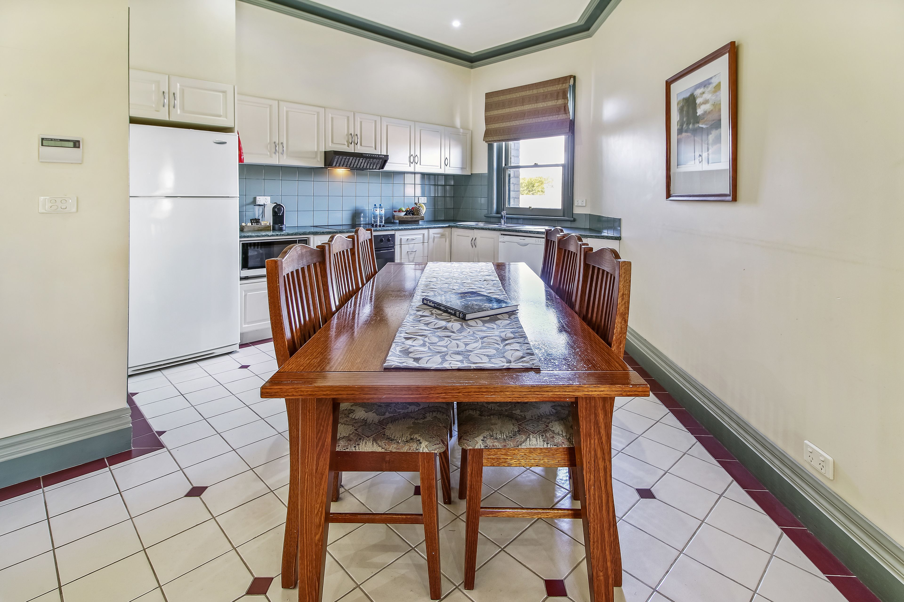 Un comedor con mesa y sillas de madera, suelo de baldosas y armarios blancos.