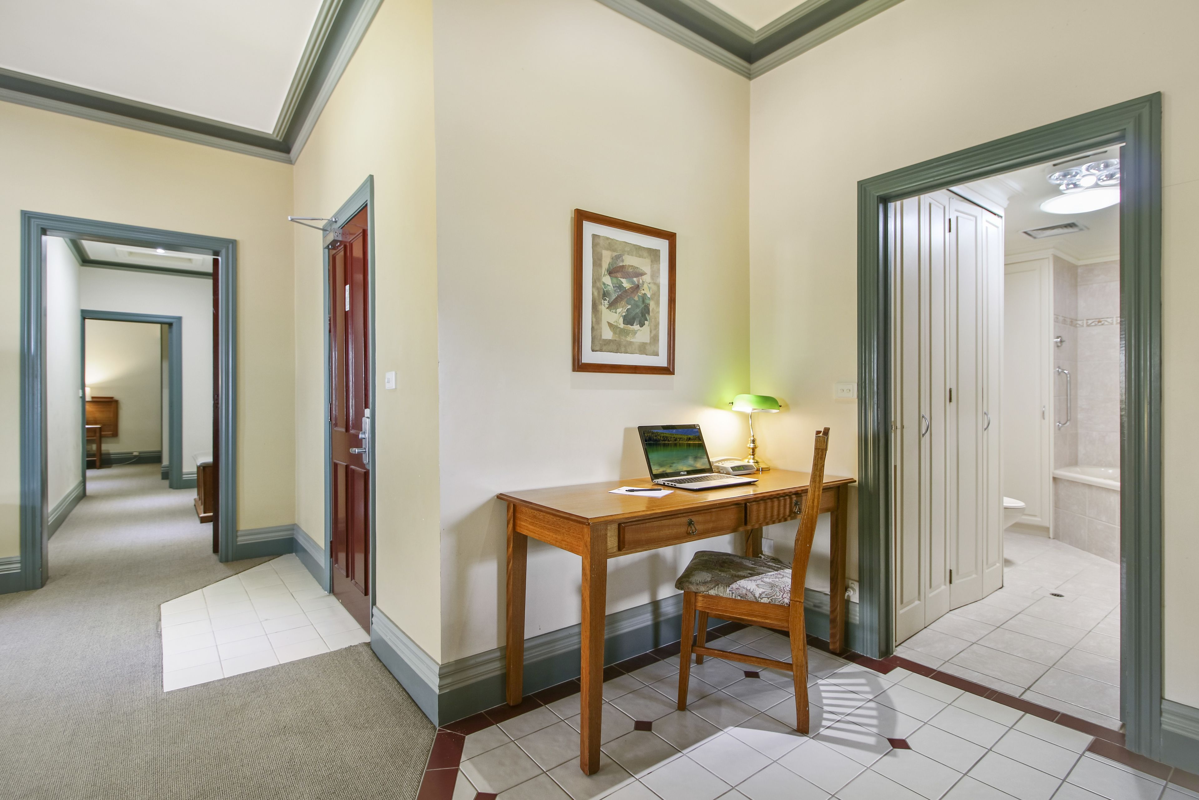 A hallway with a wooden desk, chair, and a framed picture on the wall.