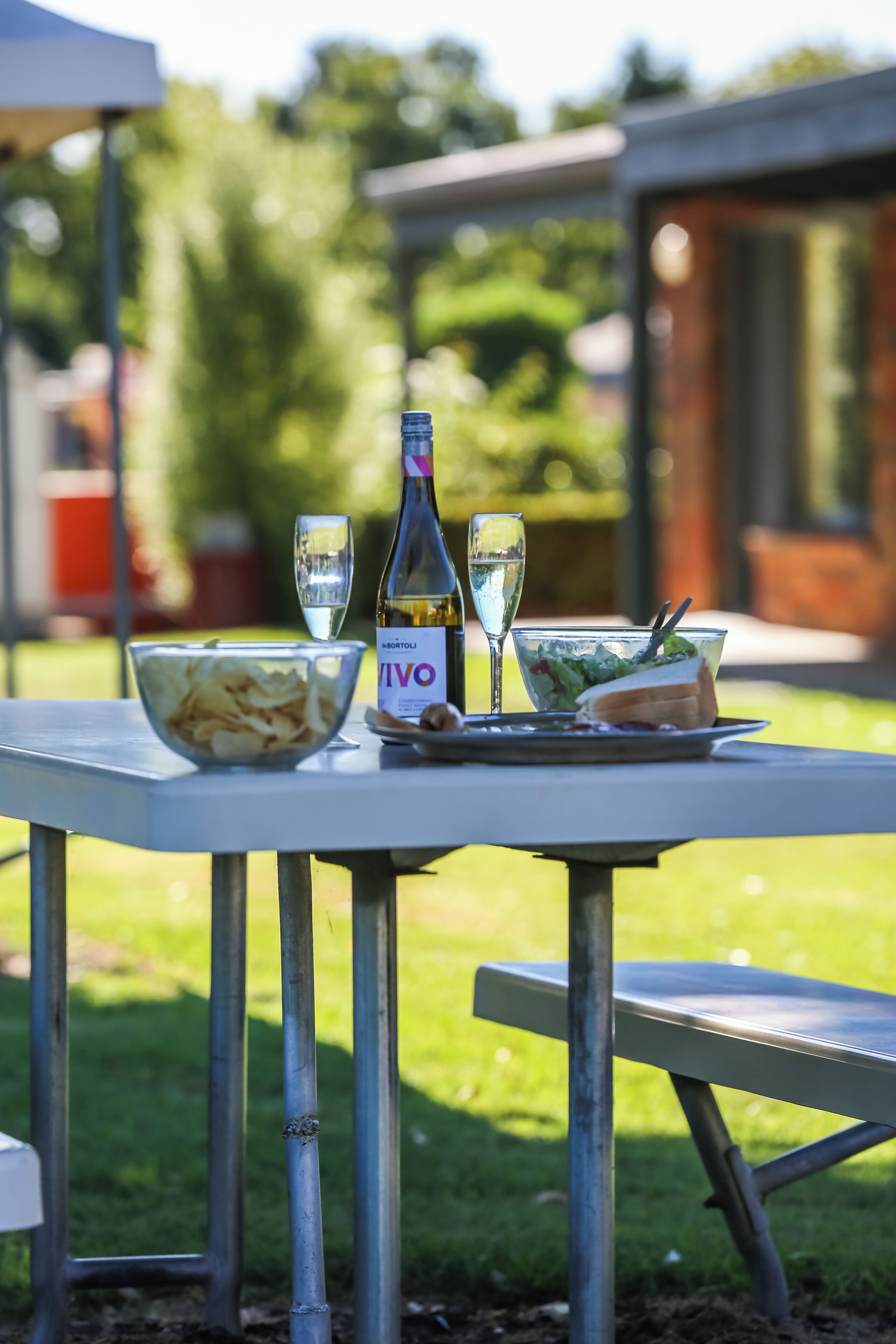 Uma mesa com uma garrafa de vinho VIVO, duas taças, um prato de batatas fritas e um sanduíche.