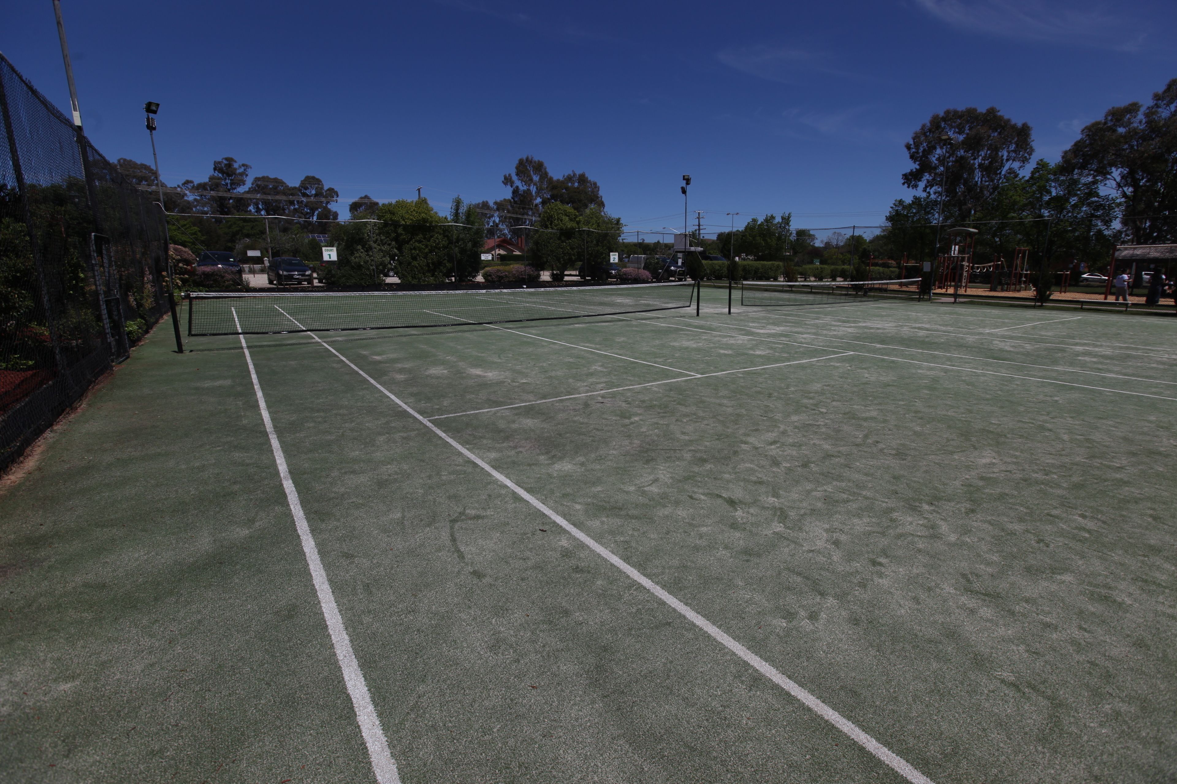 Un court de tennis avec un filet, entouré d’arbres et de bâtiments.