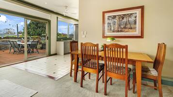 Uma área de refeições com mesa e cadeiras de madeira, um quadro na parede e vista para um pátio externo através de uma porta de vidro deslizante.