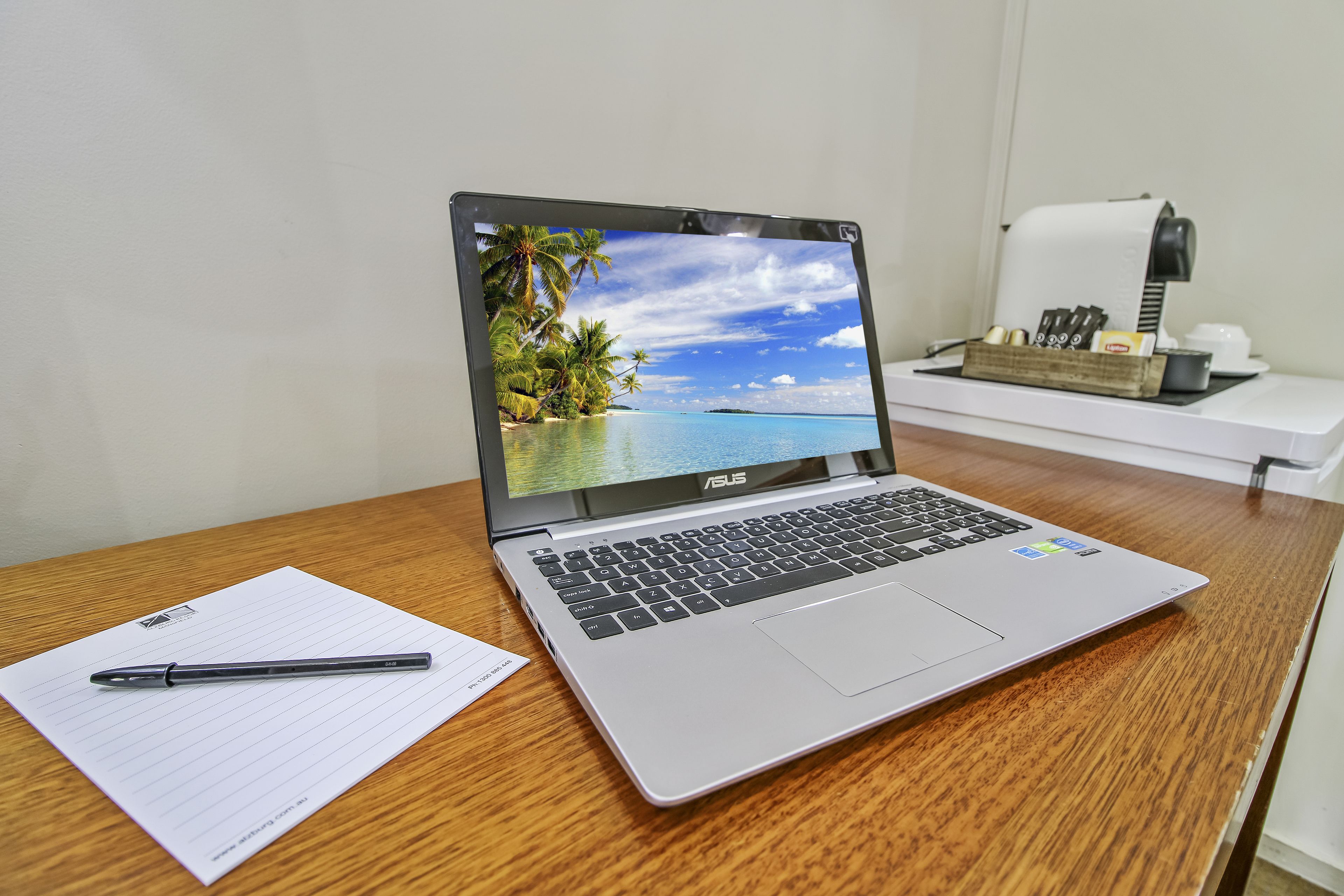 Um laptop numa secretária de madeira com uma caneta e papel ao lado.