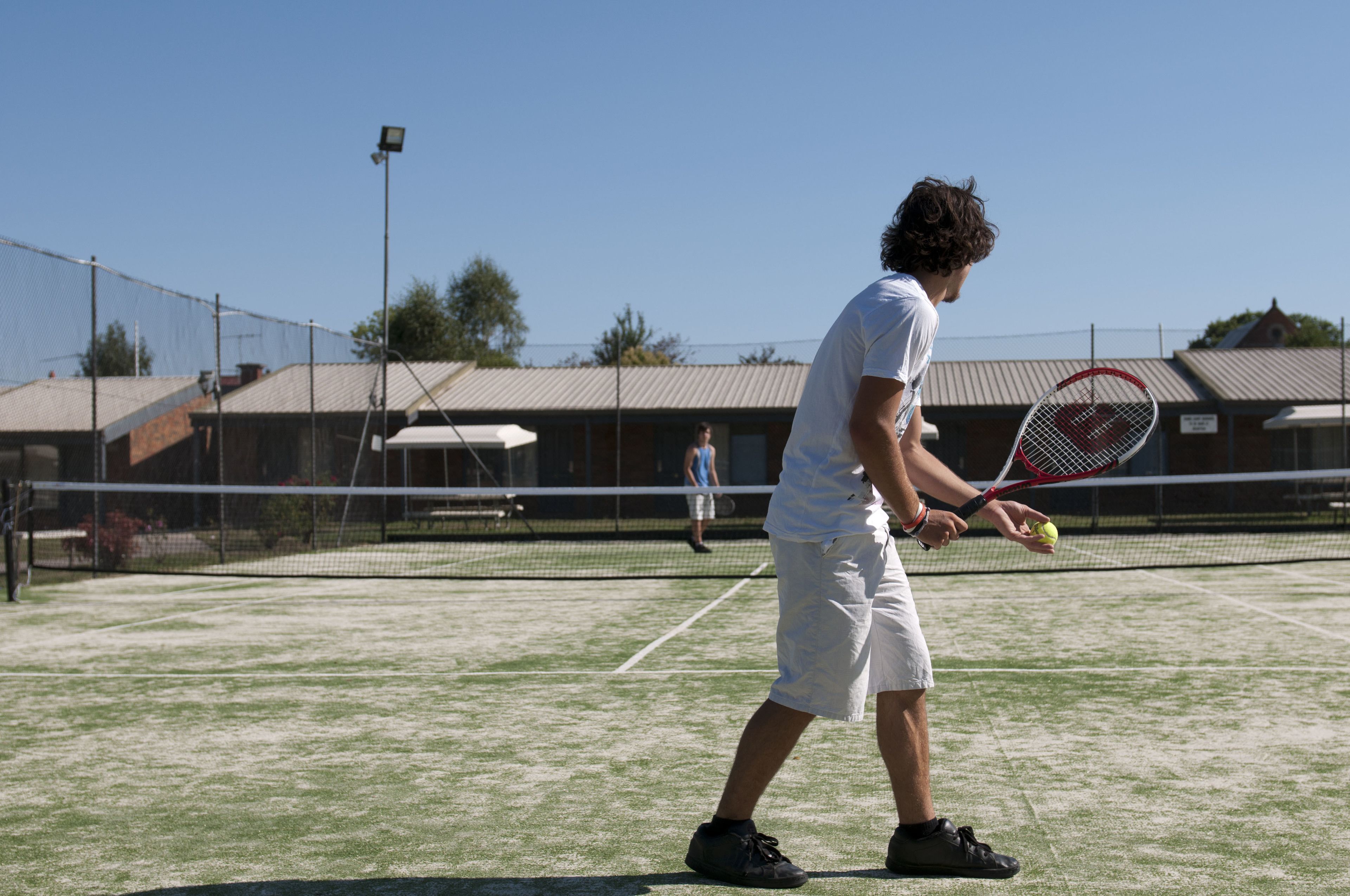 A tennis court with a net, a person holding a tennis racket, and another person in the background.